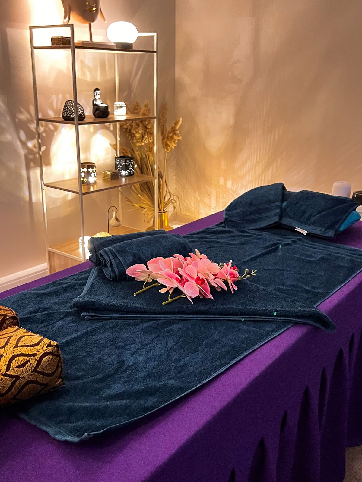 Opgemaakte behandeltafel met diepblauwe handdoeken en roze orchideeën, warm verlicht